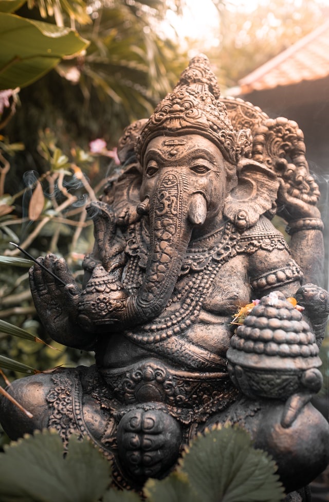 A stone Ganesha murti wreathed in incense smoke and morning light