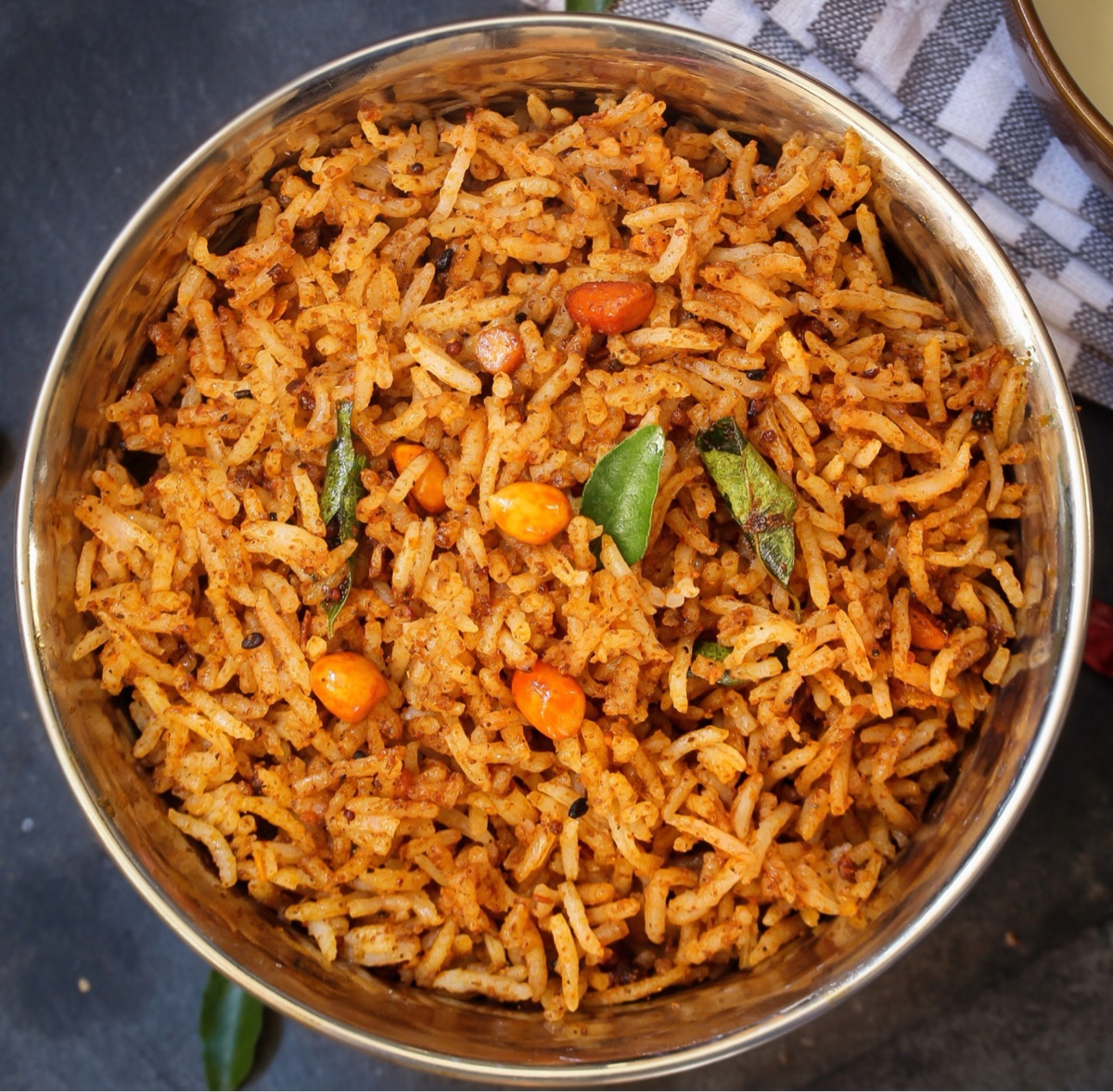 A steel bowl of freshly prepared puliyodarai prasadam, studded with peanuts and curry leaves