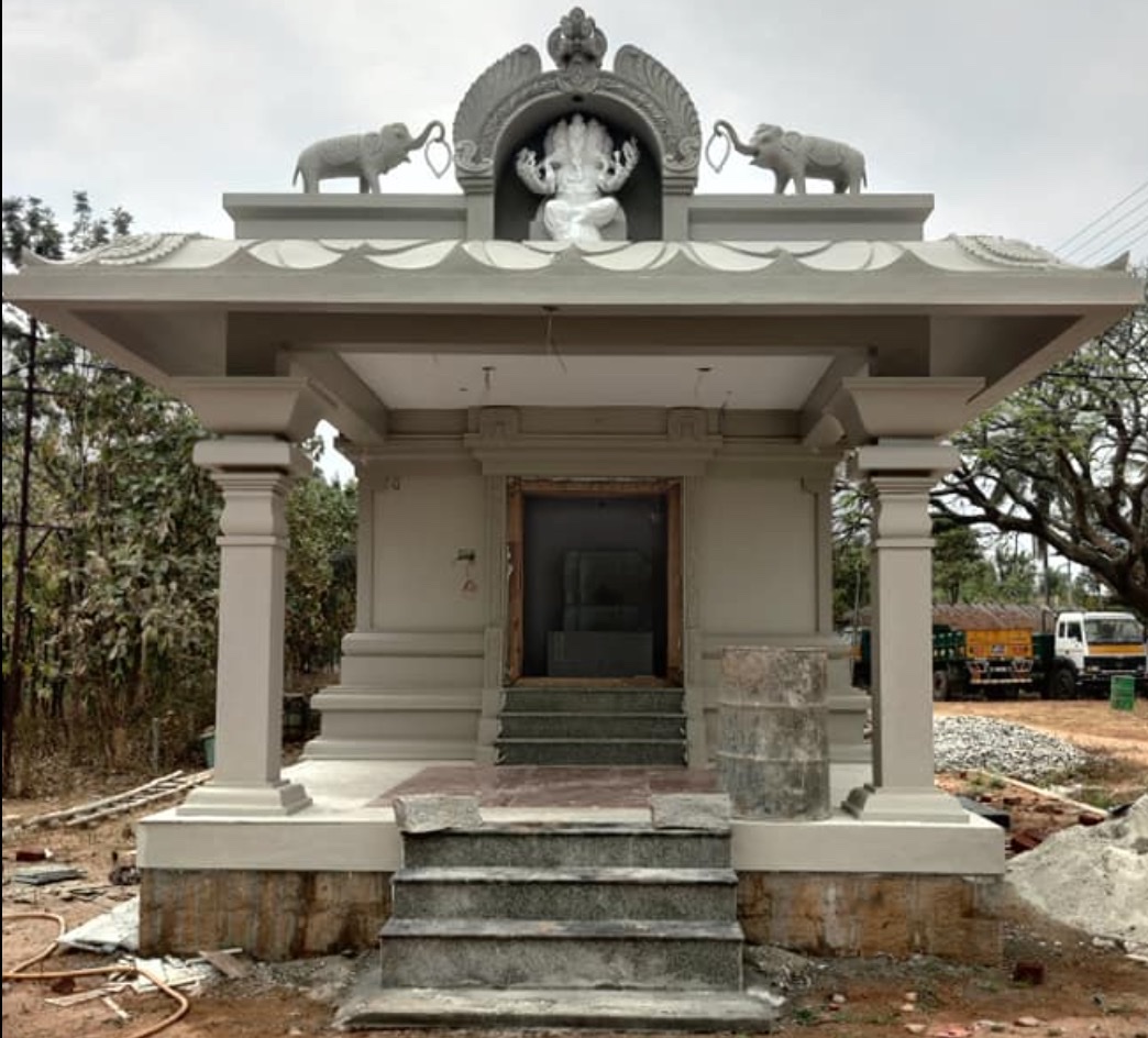 A small village temple mid-renovation: fresh stone columns, carved arch, and elephant sculptures above the entrance